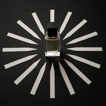 Scent strips laid in a circle on a dark table around a single bottle